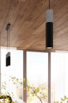 Lampa wisząca Borgio 1-punktowa w kolorze czarnym z betonowym detalem. Okrągły, wysoki korpus z czarnego metalu, zawieszony na cienkim przewodzie. W tle jasne okno z firanami, drewniane podłogi.