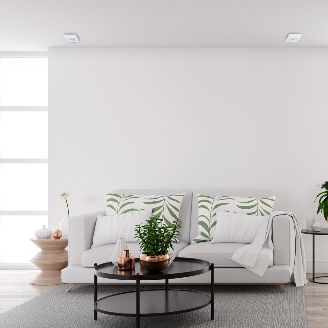 Nusa Square oprawa do zabudowy 1-punktowa w kolorze białym, zamontowana w suficie, minimalistyczny design, idealna do oświetlenia wnętrz. W tle widoczny nowoczesny salon z kanapą, stolikiem i roślinnością.