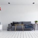 Czarna, kwadratowa oprawa do zabudowy Nusa Square, umieszczona w suficie. W tle nowoczesny salon z szarym sofą, drewnianym stolikiem i jasnymi ścianami. Oprawa o minimalistycznym designie, wkomponowana w jasne, eleganckie wnętrze.