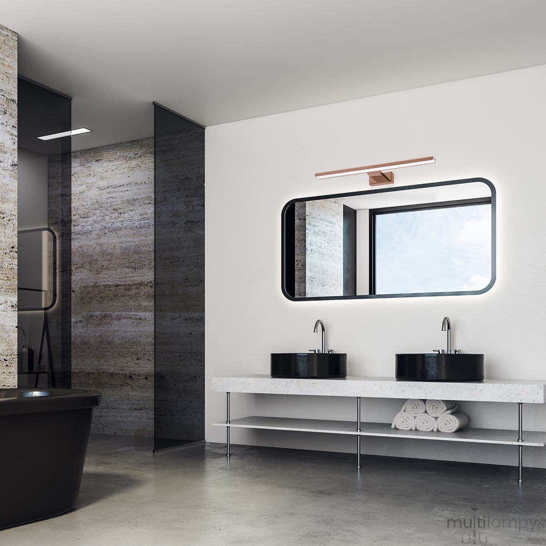 Kinkiet LED Shine IP44 w kolorze różowego złota, montowany nad lustrem. Posiada prostokątną podstawę i emitującą światło oprawę, umieszczony na jasnej ścianie w nowoczesnej łazience z czarnymi umywalkami i dużym lustrem.