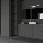 Kinkiet Shine LED IP44 w kolorze różowego złota, o długości 60 cm i mocy 13,8W, zamontowany nad umywalką w nowoczesnej łazience. Oświetlenie jest zamocowane na ciemnej ścianie, obok lusterka i zestawu kosmetyków.