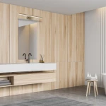 Kinkiet Shine LED IP44 w mosiężnym wykończeniu, umieszczony nad lustrem w nowoczesnej łazience. Kinkiet ma prostokątny kształt i emitowane ciepłe światło, idealny do oświetlenia strefy umywalki. Tło w jasnym drewnie i szarej podłodze.