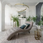Złota lampa wisząca Lucero LED 1-punktowa, z dwoma okręgami, zawieszona we wnętrzu. Lampa znajduje się nad eleganckim fotelem w kształcie fali, otoczona roślinami oraz dekoracyjnymi elementami. Tło w jasnych kolorach, z detalami architektonicznymi.