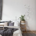Lampa wisząca Rings LED 6-punktowa w kolorze chromu, składająca się z sześciu okrągłych elementów. Zawieszona nad łóżkiem, w nowoczesnej aranżacji sypialni z rośliną w doniczce i poduszkami w odcieniach szarości.