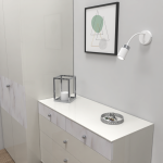 Kinkiet Joker Flex 1-punktowy w kolorze białym, z elastycznym ramieniem, zamontowany na ścianie obok minimalistycznego obrazu. W tle widoczna komoda z lustrzanym blatem, szklana latarnia i okrągła miska z akcesoriami.