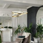 Złota lampa wisząca Float LED, składająca się z dwóch okrągłych pierścieni, wisi w eleganckim wnętrzu z roślinami. Lampa zawieszona na cienkich linkach, w tle widoczny kominek i dekoracyjne elementy architektoniczne.