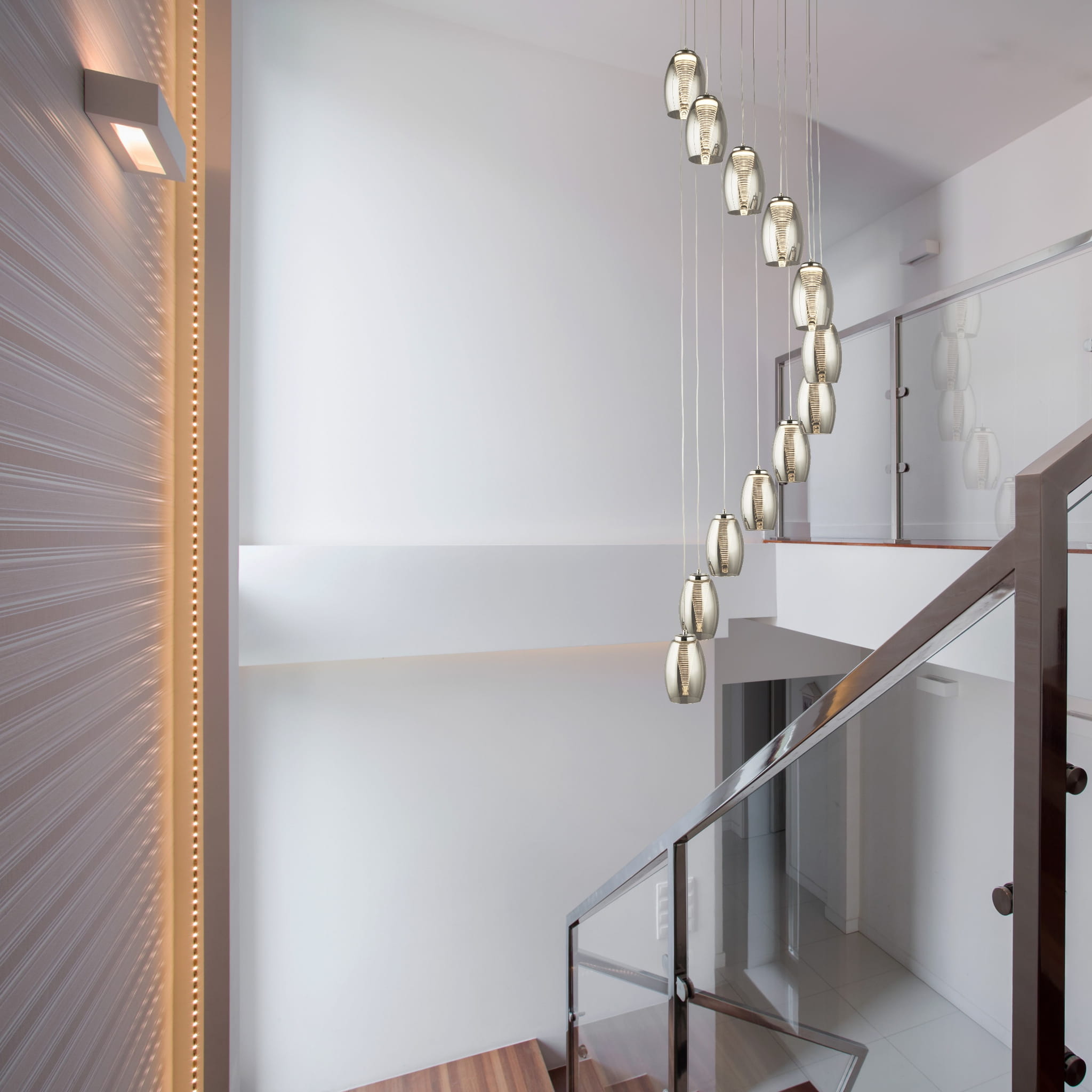 Lampa wisząca Cyclone LED 12-punktowa w kolorze chromu z przydymionymi kloszami, zawieszona na cienkich linkach, w kształcie owalnych tub. Widoczna w aranżacji wnętrza z drewnianymi schodami i nowoczesnym balustradą.