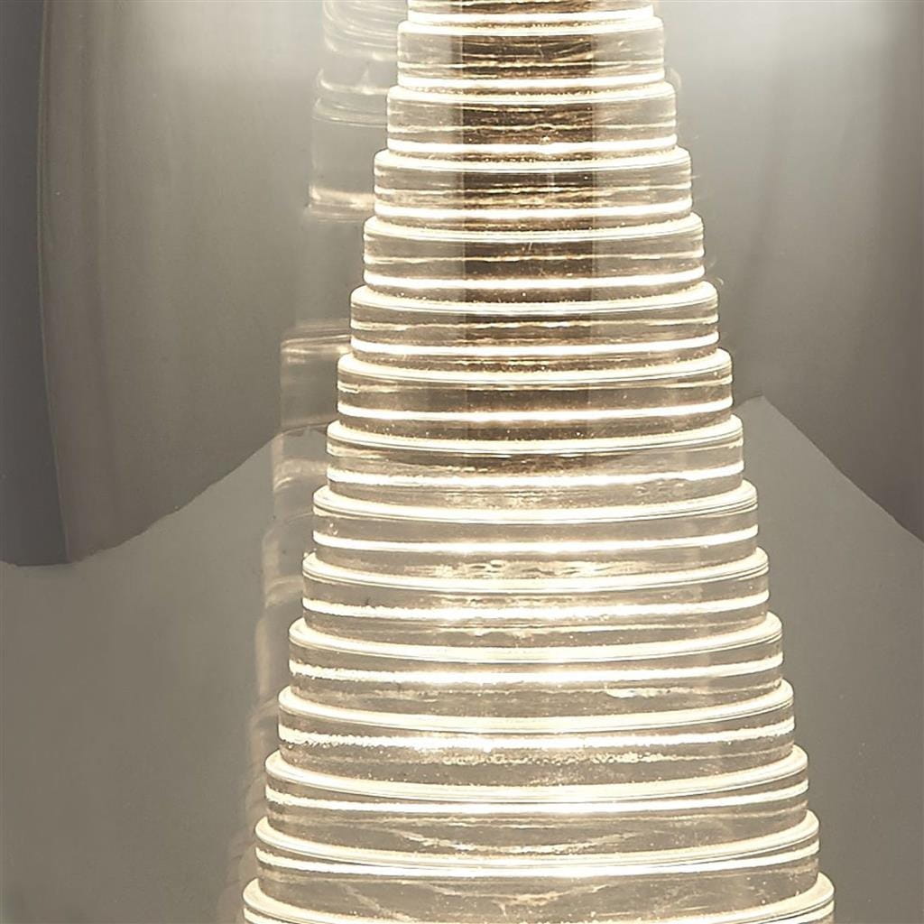 Lampa stołowa Cyclone LED w chromowanej obudowie z przydymionym szkłem, o cylindrycznym kształcie z wyraźnymi, okrągłymi detalami. Ujęcie z bliska, skupione na efekcie świetlnym i teksturze szkła.
