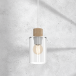 Lampa wisząca Madera 1-punktowa w kolorze białym z drewnianym detalem u góry oraz przezroczystym kloszem. Produkt zawiera żarówkę E27, zawieszony na białym przewodzie, z widocznym tłem betonowym.