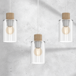 Biała lampa wisząca Madera z trzema kloszami, każdy z przezroczystego szkła, z drewnianymi uchwytami. Klosze mają okrągły kształt, a w środku widoczne żarówki. Produkt zawieszony na białych linkach, na tle szarej, teksturowanej ściany.