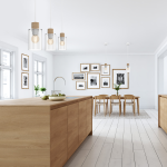 Lampa wisząca Madera 3-punktowa w kolorze białym z przezroczystymi kloszami i drewnianymi detalami, zawieszona nad drewnianym blatem kuchennym. W tle widoczne zdjęcia w ramach i stół z krzesłami.