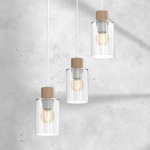 Lampa wisząca Madera 3-punktowa w białym kolorze. Trzy przezroczyste klosze szklane z drewnianymi elementami na górze. Długo wiszące przewody. Tło w odcieniach szarości. Idealna do nowoczesnych wnętrz.