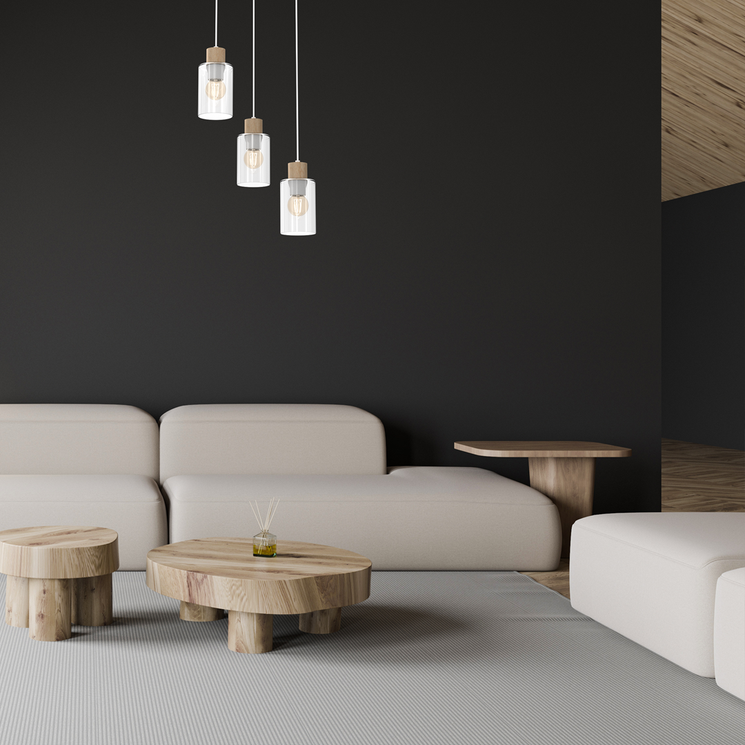 Lampa wisząca 3-punktowa Madera w białym kolorze, z transparentnymi kloszami i drewnianymi detalami, zawieszona nad jasnym, minimalistycznym wnętrzem z kanapą i stołem kawowym z naturalnego drewna. Tło ciemne, podkreślające elegancję lampy.