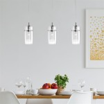 Lampa wisząca Duo I w kolorze chromowanym z trzema przezroczystymi kloszami, zawieszona nad drewnianym stołem. Produkt o cylindrycznym kształcie, montowany na cienkich linkach, w tle stół z owocami i naczyniami, na jasnym tle.