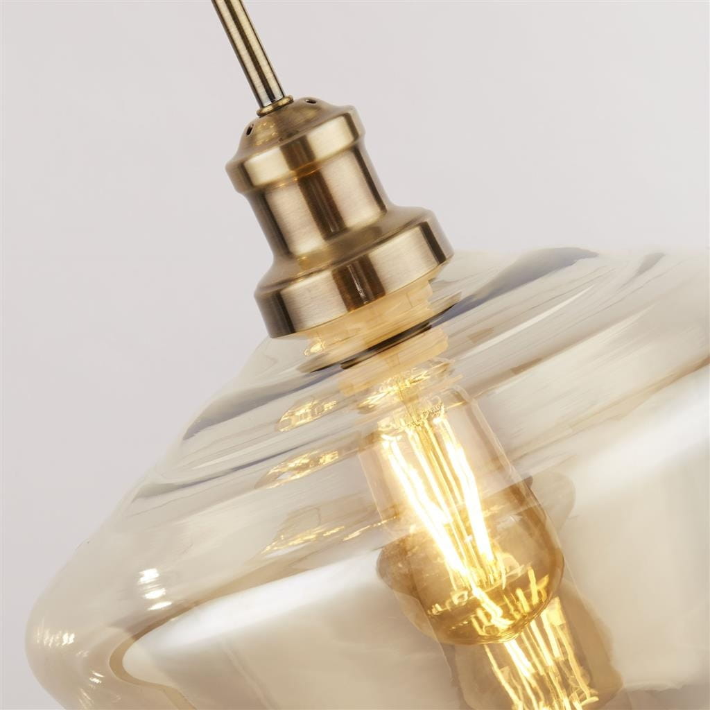 Lampa wisząca Mia 3-punktowa w kolorze antycznego mosiądzu z przezroczystym kloszem. Widoczny detal mocowania z mosiądzu oraz żarówka w środku, na tle jasnym. Idealna do nowoczesnych wnętrz.