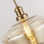 Lampa wisząca Mia 3-punktowa w kolorze antycznego mosiądzu z przezroczystym kloszem. Widoczny detal mocowania z mosiądzu oraz żarówka w środku, na tle jasnym. Idealna do nowoczesnych wnętrz.