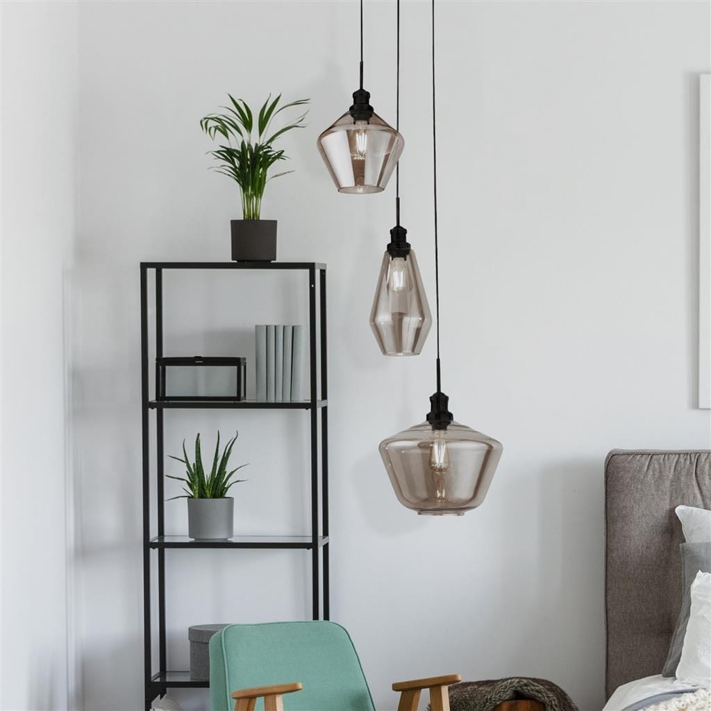 Lampa wisząca 3-punktowa Mia w czarnym kolorze, z przezroczystymi kloszami o geometrycznych kształtach, zawieszona na czarnych linkach. W tle regał z rośliną i książkami, neutralne, jasne tło.