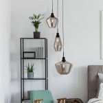 Lampa wisząca 3-punktowa Mia w czarnym kolorze, z przezroczystymi kloszami o geometrycznych kształtach, zawieszona na czarnych linkach. W tle regał z rośliną i książkami, neutralne, jasne tło.