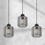 Lampa wisząca Sombra 3-punktowa, czarna z dymionymi kloszami. Klosze mają okrągły kształt, przymocowane do czarnych kabli. Widoczne żarówki o klasycznym kształcie, zawieszone w równych odstępach. Tło w odcieniach szarości.