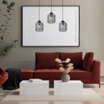 Lampa wisząca Sombra 3-punktowa w kolorze czarnym z dymionymi kloszami, zawieszona nad białymi stolikami. Klosze mają cylindryczny kształt, a ich przezroczystość podkreśla źródło światła, tworząc nowoczesny akcent w aranżacji salonu.