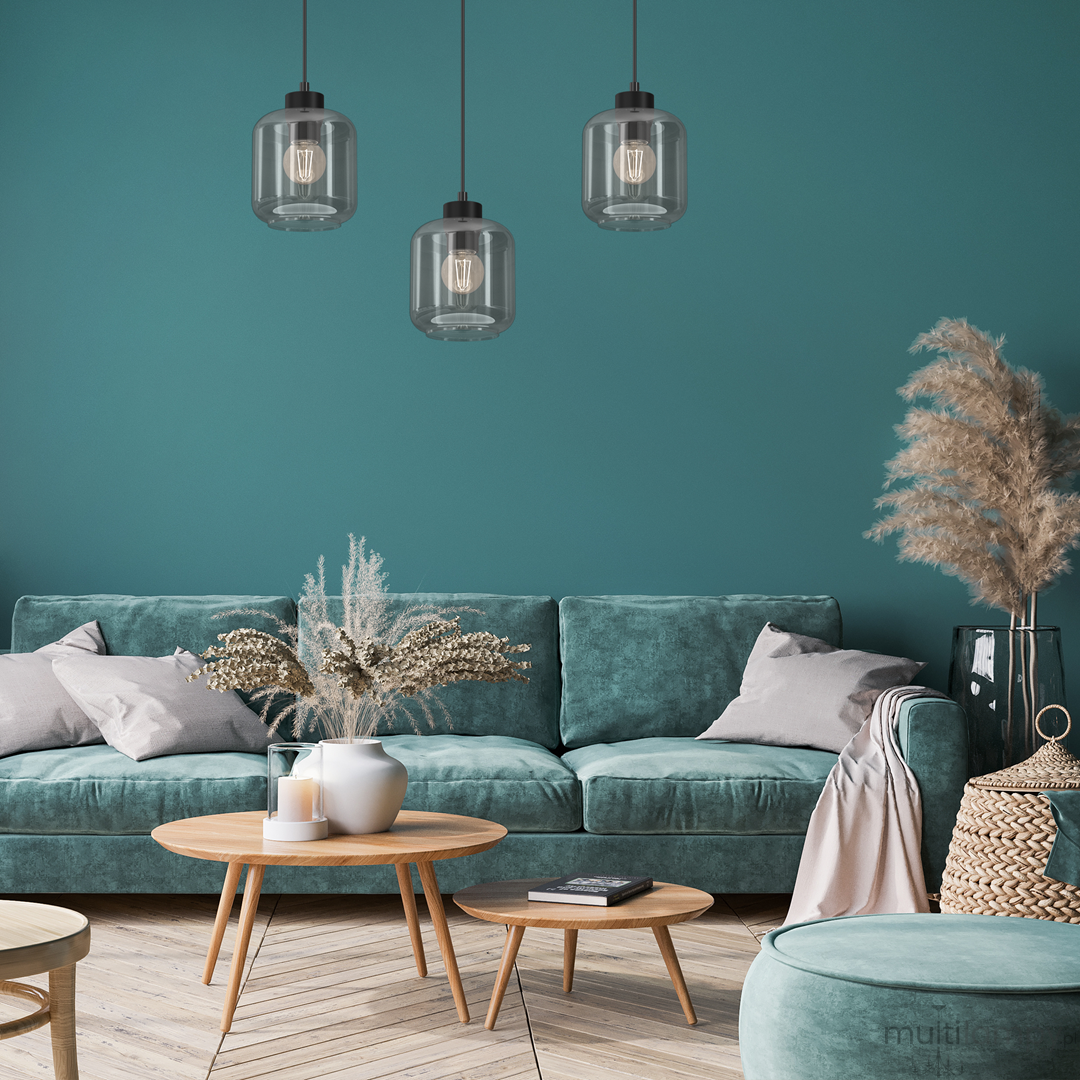 Lampa wisząca 3-punktowa Sombra w kolorze czarnym z dymionymi kloszami, zawieszona nad sofą w turkusowym kolorze. Klosze mają okrągły kształt, a w ich wnętrzu widoczne są żarówki. Tło w odcieniu zielonym, z dodatkami roślinnymi.