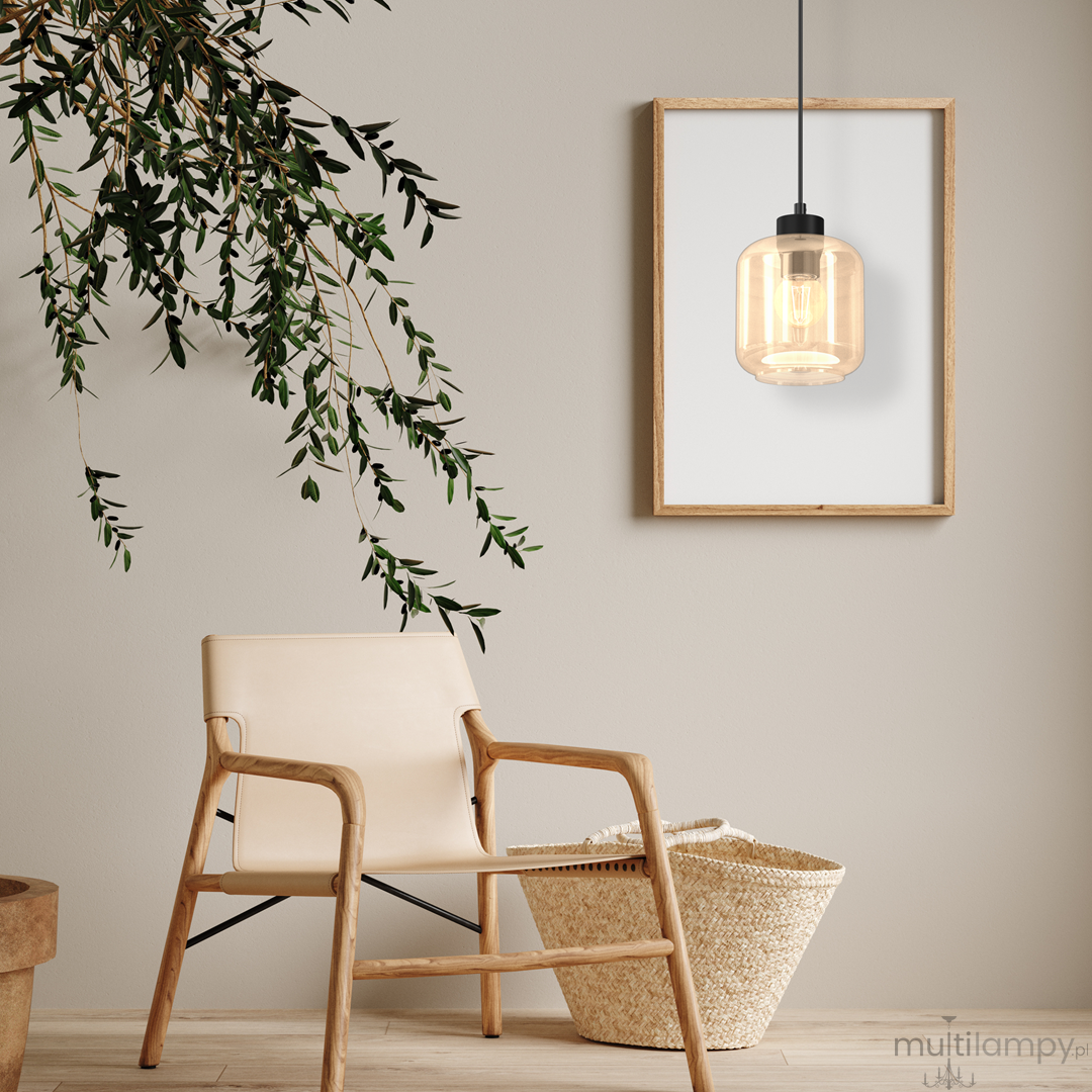 Lampa wisząca Sombra 1-punktowa w kolorze czarnym z bursztynowym kloszem, zawieszona na czarnym kablu. Otoczona nowoczesnym wnętrzem z drewnianym krzesłem, koszem i roślinnością w tle.