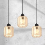 Lampa wisząca Sombra 3-punktowa w kolorze czarnym i bursztynowym. Szklane klosze w kształcie cylindrów z widocznymi żarówkami, zawieszone na czarnych przewodach. Tło w odcieniu szaro-białym.