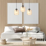 Lampa wisząca 3-punktowa Sombra w kolorze czarnym z bursztynowym kloszem, zawieszona nad jasną sofą, w nowoczesnym wnętrzu z drewnianymi panelami. Widać trzy szklane klosze i elementy dekoracyjne, takie jak stół i poduszki.