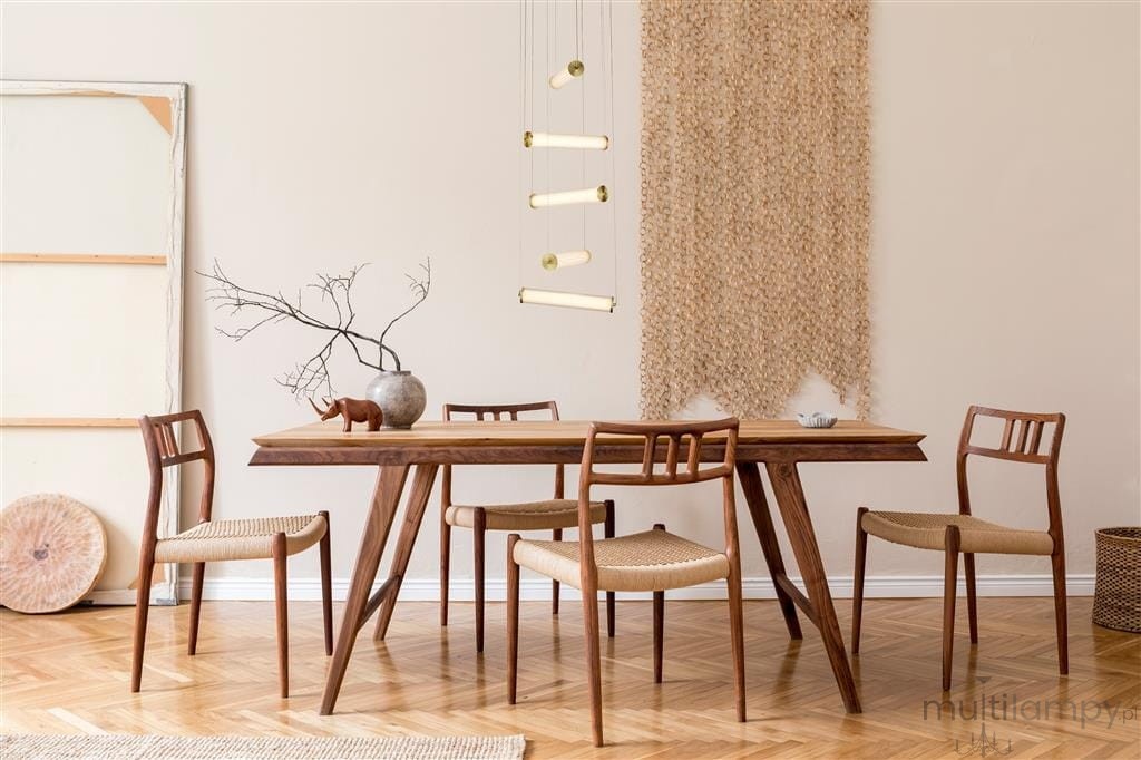 Lampa wisząca Clamp LED w kolorze złotym, pięciopunktowa, zawieszona nad drewnianym stołem. W tle widoczna naturalna dekoracja ścienna oraz minimalistyczne elementy aranżacji, takie jak gałązka w wazonie i krzesła z plecionką.