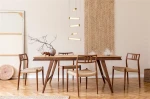 Lampa wisząca Clamp LED w kolorze złotym, pięciopunktowa, zawieszona nad drewnianym stołem. W tle widoczna naturalna dekoracja ścienna oraz minimalistyczne elementy aranżacji, takie jak gałązka w wazonie i krzesła z plecionką.