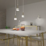 Lampa wisząca Arena 3-punktowa w kolorze białym i złotym, zawieszona nad stołem. Składa się z trzech cylindrycznych kloszy z białego materiału na złotych stelażach. W tle widoczny stół z deserem, szklankami i dzbankiem.