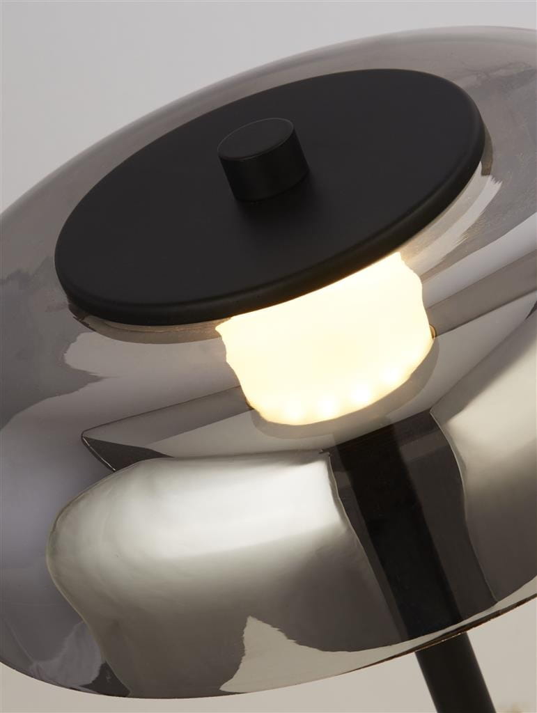 Czarna lampa stołowa LED Frisbee z metalowym kloszem, z widocznym przyciskiem w górnej części. Światło emituje ciepły blask, a połysk klosza odbija otoczenie, tworząc elegancki efekt wizualny. Produkt ujęty z góry, ukazujący detale konstrukcji.