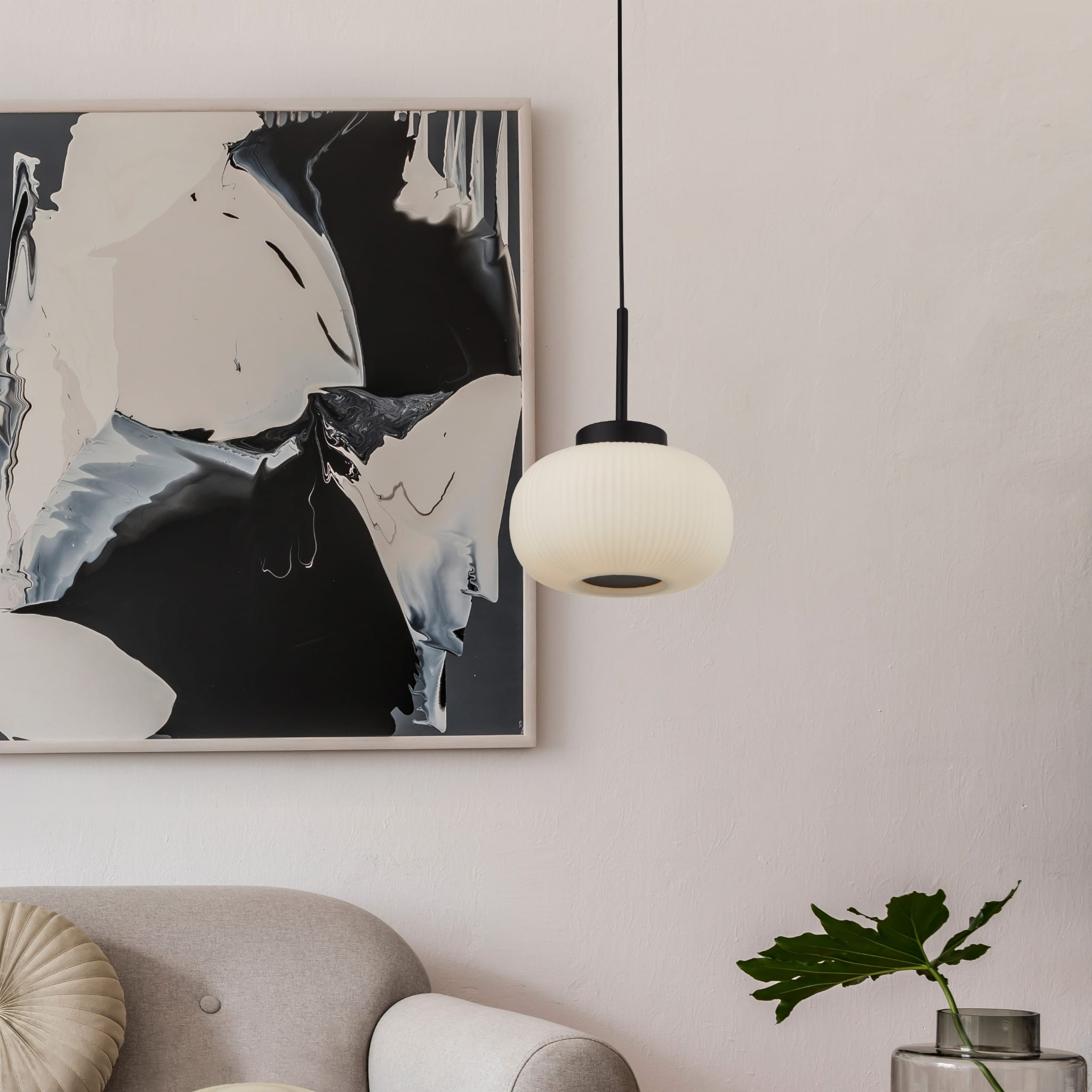 Lampa wisząca Lumina 1-punktowa w kolorze czarnym z białym kloszem. Okrągły kształt z żebrowaną fakturą, zawieszona na cienkim kablu. W tle widoczny nowoczesny obraz oraz szara sofa z dekoracyjną poduszką.