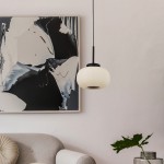 Lampa wisząca Lumina 1-punktowa w kolorze czarnym z białym kloszem. Okrągły kształt z żebrowaną fakturą, zawieszona na cienkim kablu. W tle widoczny nowoczesny obraz oraz szara sofa z dekoracyjną poduszką.