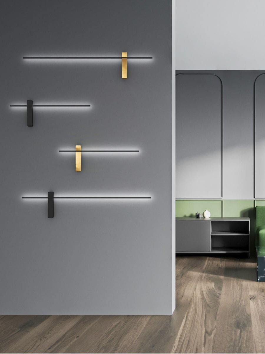 Kinkiet Bene Parette Nero/Gold 60 LED w kolorze czarnym i złotym, zamontowany na szarej ścianie, z minimalistycznym designem. W zestawie widoczne są także inne kinkiety w różnych kolorach, o prostych, geometrycznych kształtach.