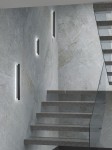 Kinkiet Ante Nero 60 LED w kolorze czarnym, zamontowany na ścianie, o prostej, smukłej formie. Oświetlenie skierowane w dół, idealne do korytarza. W tle widoczne schody i surowa, teksturowana ściana.