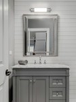 Kinkiet Omi Parette Cromo 30 IP44 LED w chromie, zamontowany nad lustrem w łazience. Oświetlenie w formie prostokątnej tuby, emitujące jasne światło, na tle szarych paneli i białego lustra. Na umywalce widoczny ręcznik.