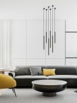 Lampa wisząca Q I Nero/Gold 60 w kolorze czarnym i złotym z sześcioma długimi, smukłymi ramionami. Zawieszona w nowoczesnym wnętrzu z szarym sofą i okrągłym stołem. Tło w jasnych odcieniach, podkreślające elegancki design.