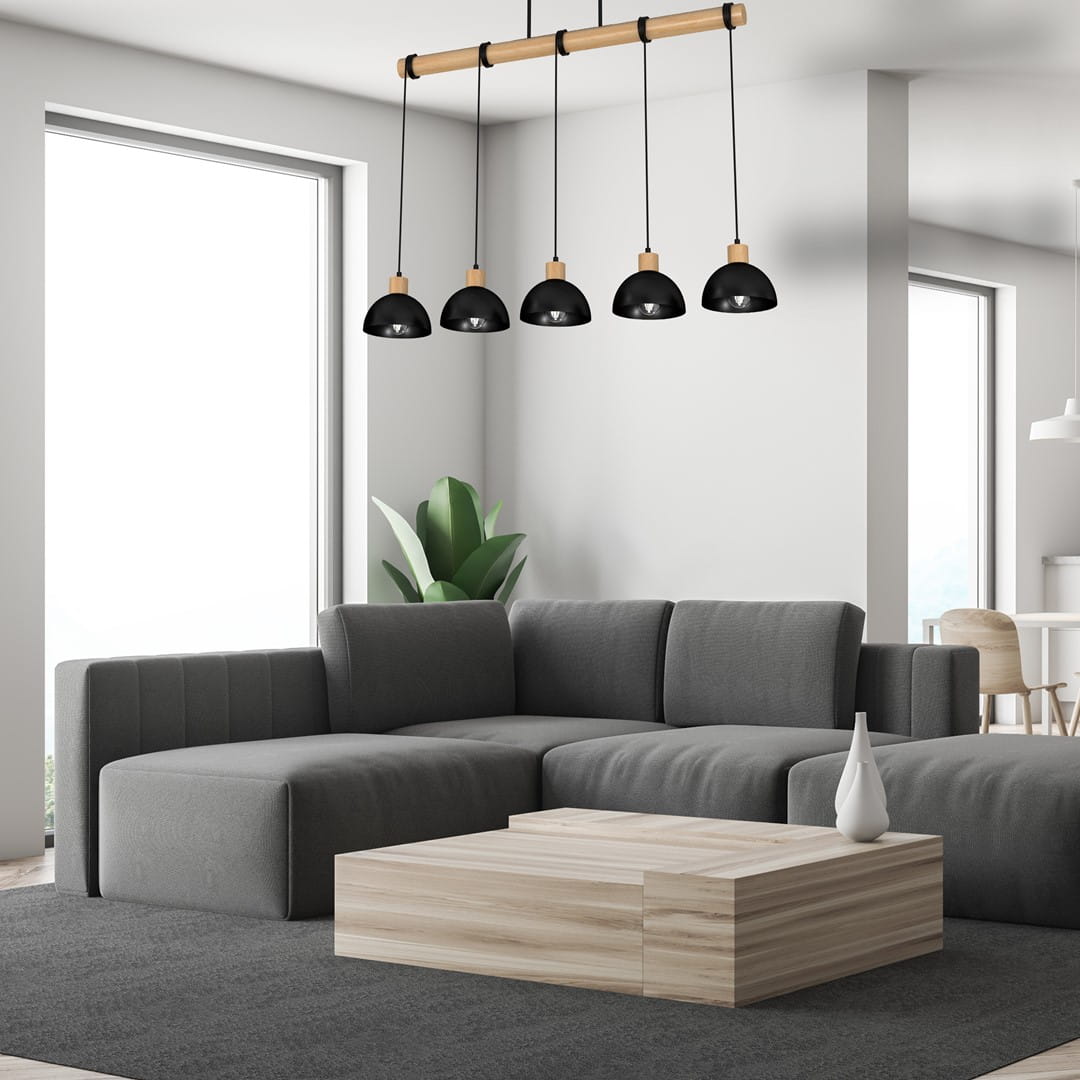 Lampa wisząca Erik 5-punktowa z czarnymi kloszami i naturalnym drewnianym uchwytem, zawieszona nad szarym narożnikiem w nowoczesnym wnętrzu. Jasne tło z oknem oraz zielona roślina dodają aranżacji świeżości.