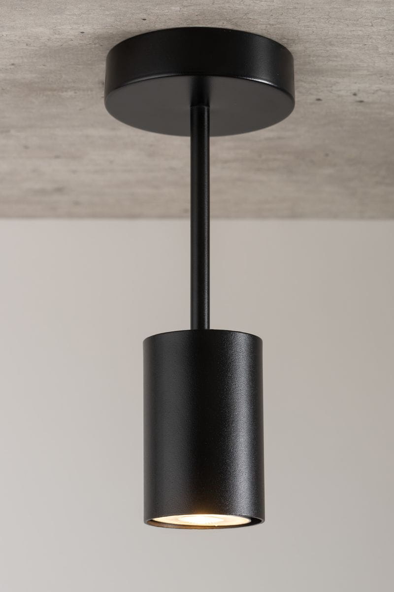 Czarna lampa sufitowa 1-punktowa Luis, wykonana z metalu, z cylindrycznym kloszem zawieszonym na prostym wsporniku. Ujęcie z dołu, ukazujące źródło światła. Tło jasne, minimalistyczne.