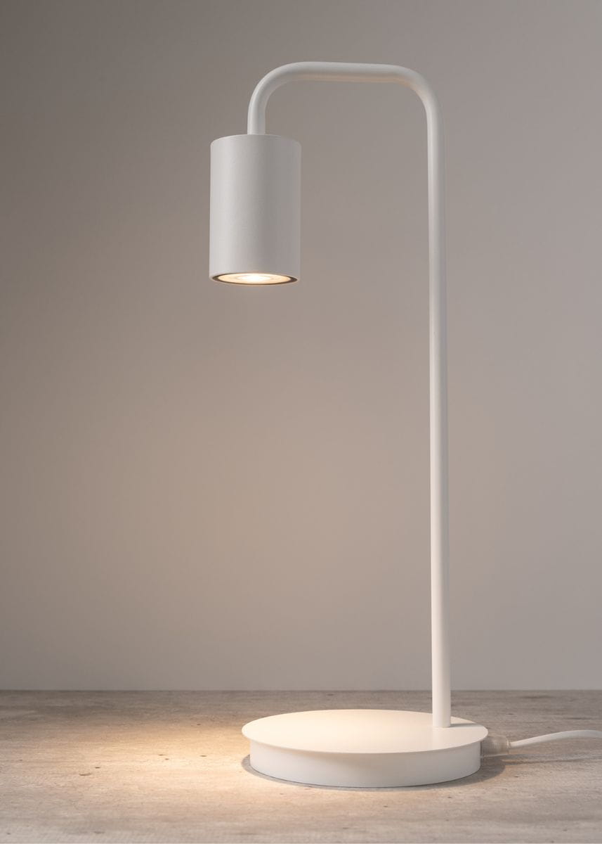 Lampa stołowa Luis 1-punktowa w kolorze białym, z okrągłą podstawą i prostą, giętą nogą. Ujęcie z boku, podkreślające cylindryczny klosz z widocznym źródłem światła. Minimalistyczny design, idealna do nowoczesnych wnętrz.