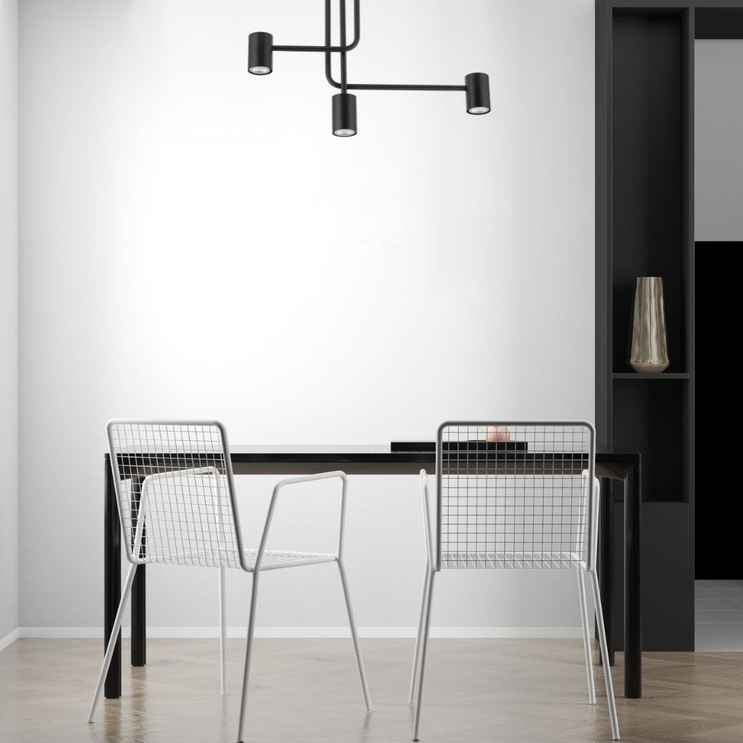 Czarna lampa sufitowa 3-punktowa Luis, z prostym, nowoczesnym designem. Zamontowana na suficie, z trzema regulowanymi źródłami światła, idealna do oświetlenia przestrzeni nad stołem. Tło jasne, minimalistyczne wnętrze z białymi krzesłami.