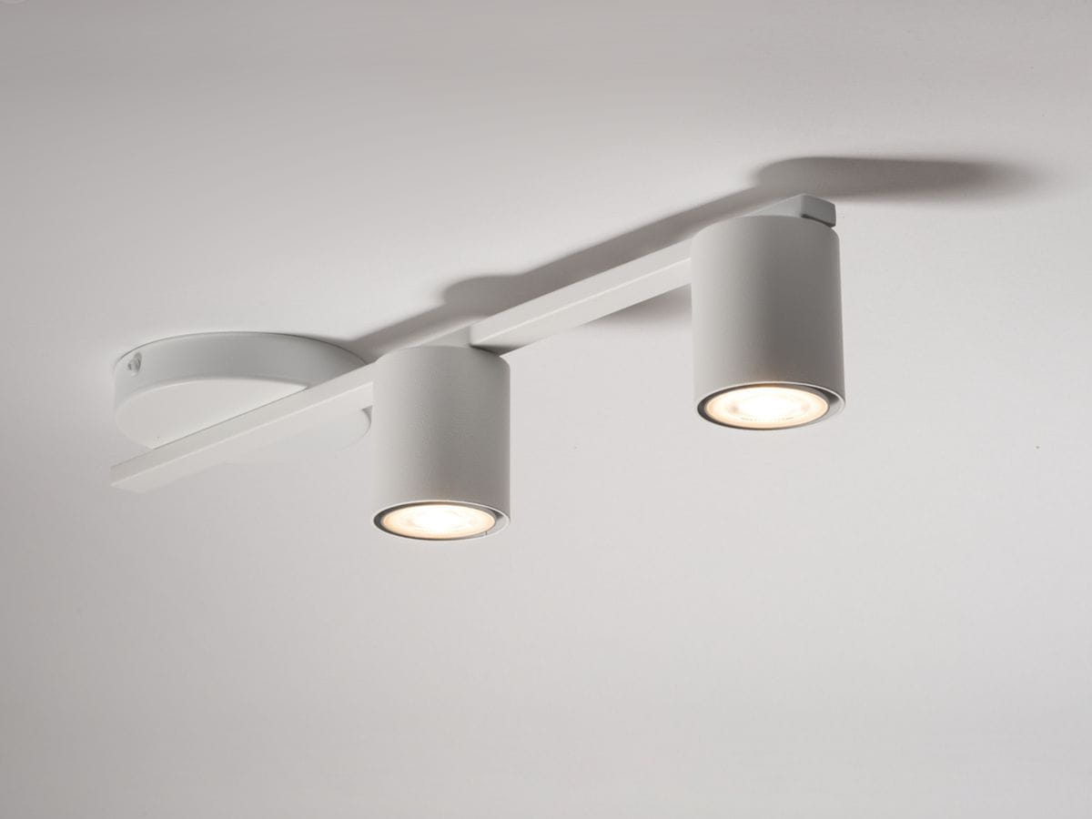 Biała lampa sufitowa 2-punktowa Sky z metalowymi cylindrami, zamontowana na prostokątnej belce. Ujęcie z góry, ukazujące dwa źródła światła oraz okrągłą podstawę. Prosty, nowoczesny design, idealna do różnych wnętrz.