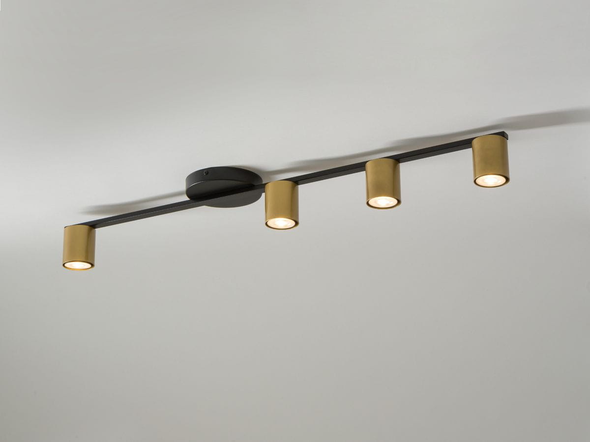 Czarna lampa sufitowa 4-punktowa z metalowymi złotymi kloszami, zamontowana na okrągłej podstawie. Klosze w formie cylinderków skierowane w dół, umieszczone na poziomej belce. Prosty, nowoczesny design, idealna do różnych wnętrz.