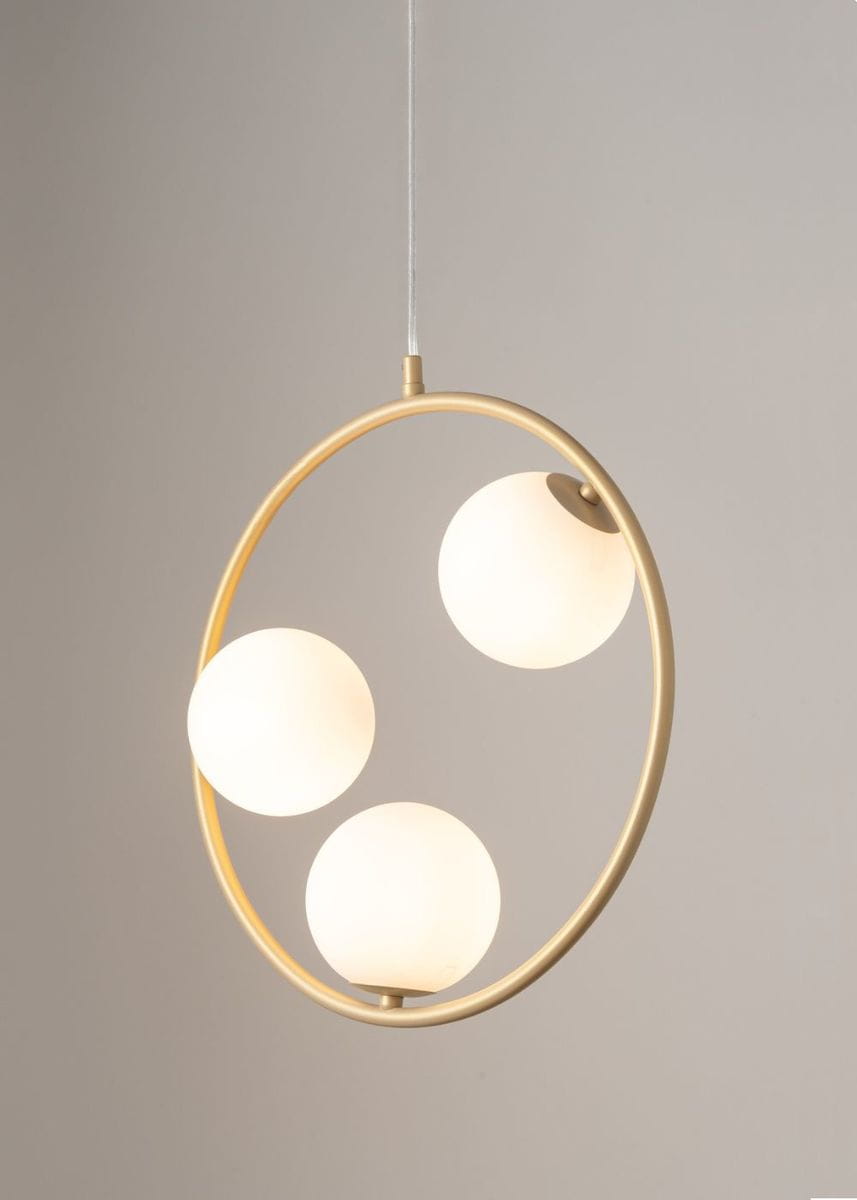 Lampa wisząca Aqua 3-punktowa w kolorze złotym z trzema białymi, okrągłymi kloszami umieszczonymi w metalowym pierścieniu. Wywieszona na przezroczystym przewodzie, z widocznym mocowaniem na górze. Tło w neutralnym kolorze.