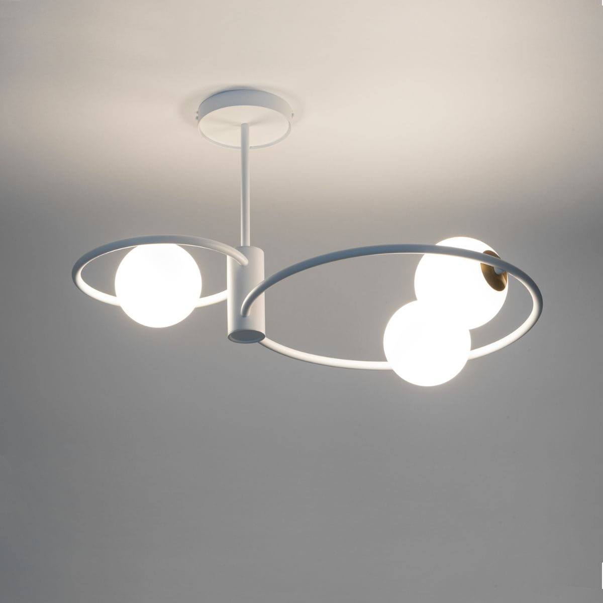 Lampa wisząca Aqua 3-punktowa w białym kolorze z okrągłymi kloszami. Stelaż w formie stylizowanych pierścieni, z centralnym mocowaniem. Klosze w kolorze białym z złotymi detalami. Ujęcie z dołu, pod kątem, na jasnym tle.