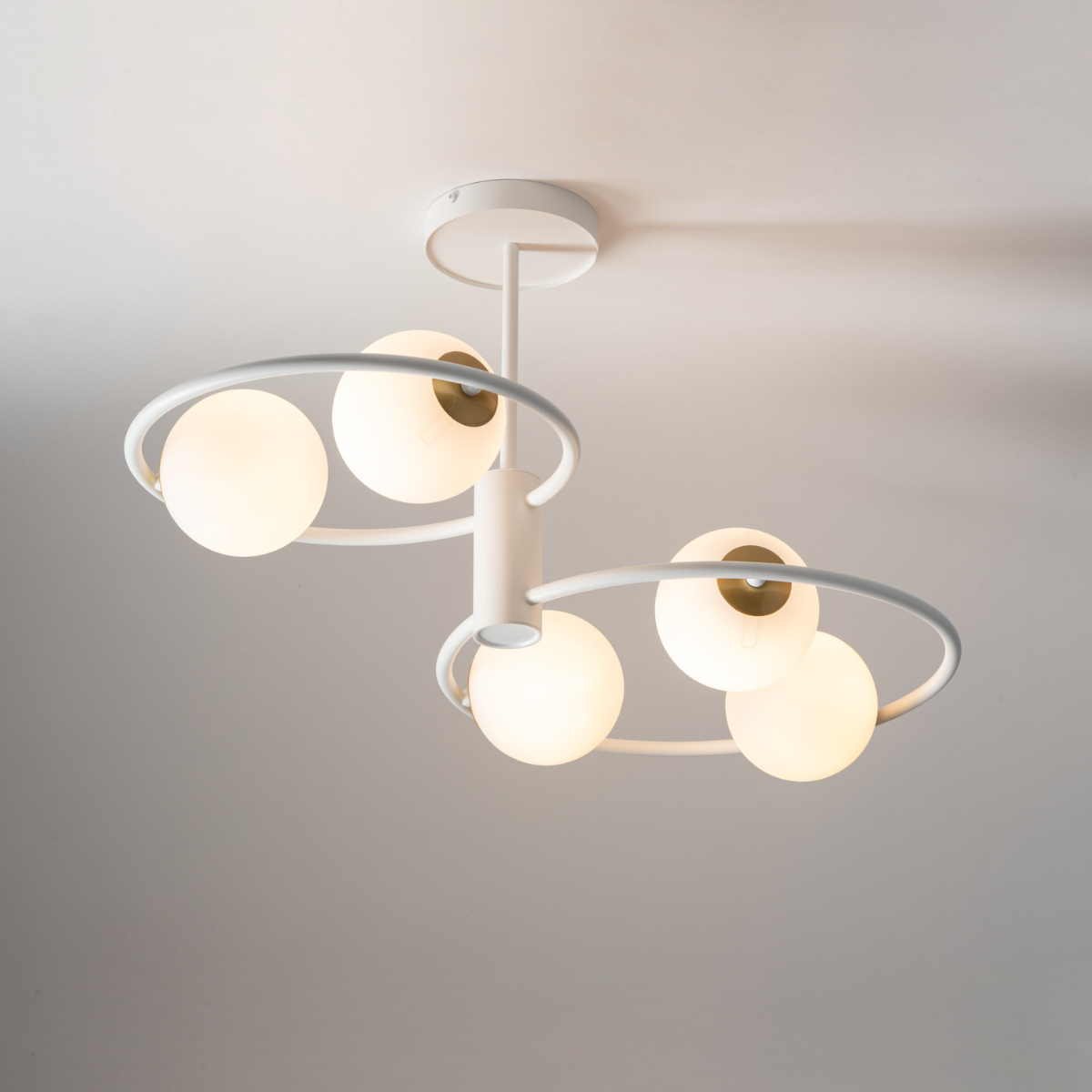 Lampa wisząca Aqua 5-punktowa w białym kolorze z złotymi akcentami. Posiada pięć okrągłych kloszy z mlecznego szkła zawieszonych na białych obręczach. Ujęcie z dołu, pokazujące szczegóły konstrukcji i rozmieszczenie źródeł światła.