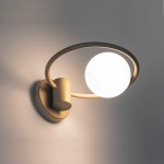 Kinkiet Aqua 1-punktowy w kolorze złotym, z okrągłym, białym kloszem. Ujęcie z boku, ukazujące elegancki, minimalistyczny design oraz metalową konstrukcję z zaokrąglonymi kształtami. Zainstalowany na gładkiej, jasnej ścianie.