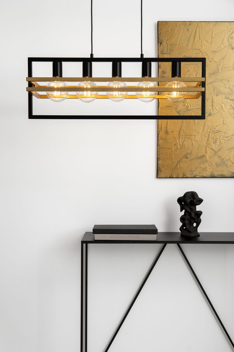 Lampa wisząca Merci 5-punktowa w kolorze czarnym i złotym. Ma prostokątną konstrukcję z pięcioma przezroczystymi żarówkami, zawieszona na cienkich przewodach. W tle widoczna złota dekoracja oraz czarna konsola z książkami i rzeźbą.