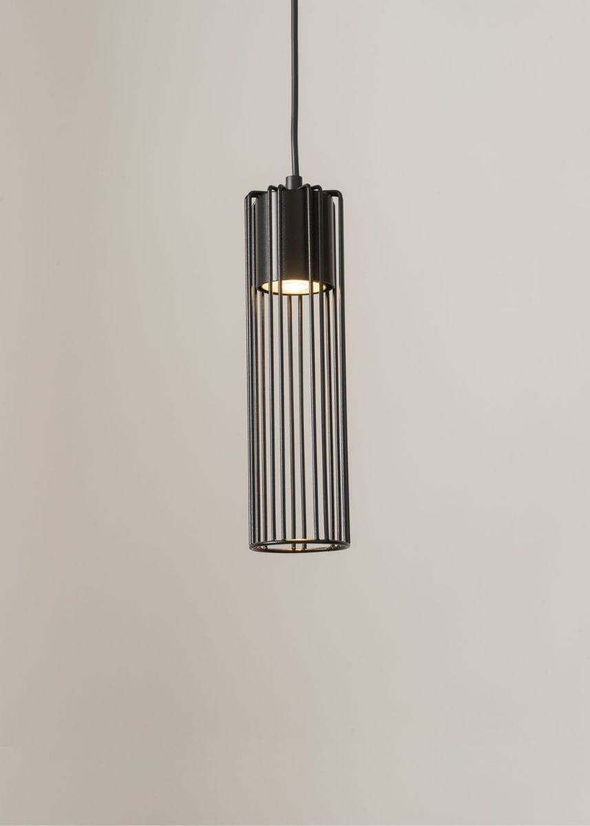 Lampa wisząca Fobia w kolorze czarnym z metalową, szczelinową osłoną, zawieszona na cienkim przewodzie. Prosta, cylindryczna forma z widoczną oprawą świetlną wewnątrz. Ujęcie frontalne, na jednolitym tle.